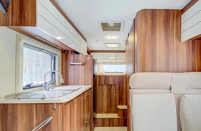 A camper van interior with wood cabinets, a sink, and a seating area.