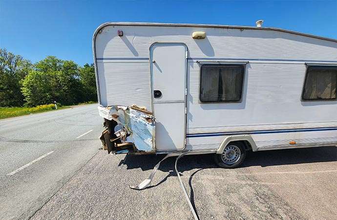 A damaged white RV is parked on the side of a road. 