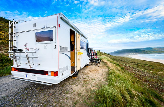 A white RV is parked on a cliff overlooking a beach.