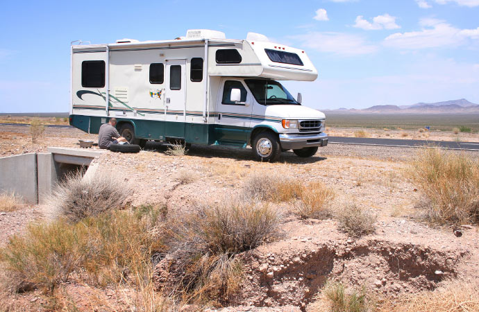 Man stranded on roadside, looking at detached RV wheel